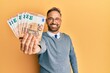 © Krakenimages.com - Handsome middle age man holding bunch of euros looking positive and happy standing and smiling with a confident smile showing teeth