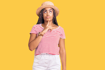 Sticker - Young african american woman with braids wearing summer hat thinking concentrated about doubt with finger on chin and looking up wondering