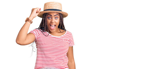 Canvas Print - Young african american woman with braids wearing summer hat angry and mad raising fist frustrated and furious while shouting with anger. rage and aggressive concept.