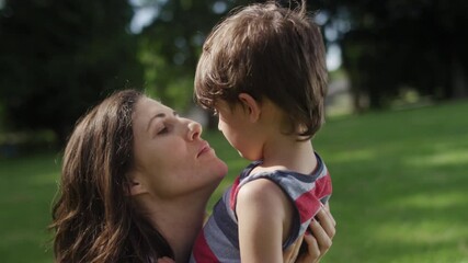 close-up of a beautiful mother kissing her young son at the park