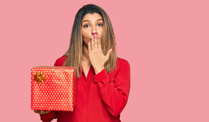 Sticker - Beautiful brunette woman holding gift covering mouth with hand, shocked and afraid for mistake. surprised expression