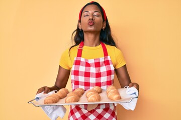 Wall Mural - Young indian girl wearing baker uniform holding homemade bread looking at the camera blowing a kiss being lovely and sexy. love expression.