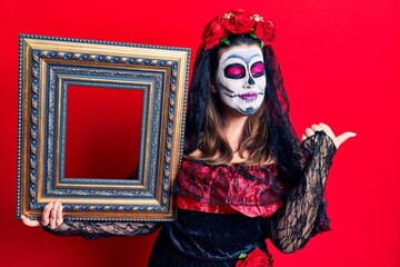 Poster - Young woman wearing day of the dead costume holding empty frame pointing thumb up to the side smiling happy with open mouth