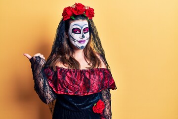 Poster - Young woman wearing day of the dead costume over yellow smiling with happy face looking and pointing to the side with thumb up.