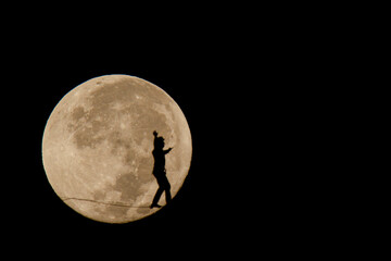  silhouette of a young man walking a tightrope in landscape and in the background the full moon