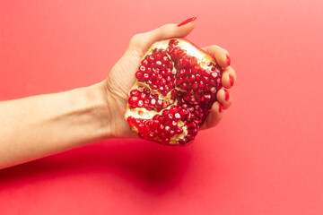 Red fresh pomegranate in woman's hand on red background. Copy space.