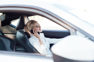 Beautiful female blonde driver talking smartphone behind the wheel of car