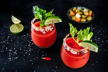 Bloody Mary cocktails on a black background, with lime and celery, served with pickles