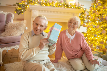 Wall Mural - Elderly man holding christmas gift from his wife and looking interested