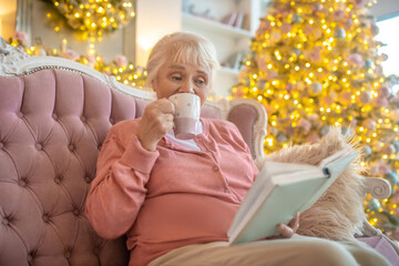 Grey-haired woman reading a book and drinking tea