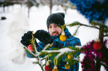Close-up Of Young Man Putting Red Bauble On Tree During Winter