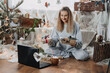 © irissca - Christmas online remote celebration, virtual gathering. Christmas Holidays in the Time of lockdown, COVID Pandemic, new normal time. Happy woman celebrating xmas and meeting via internet near laptop