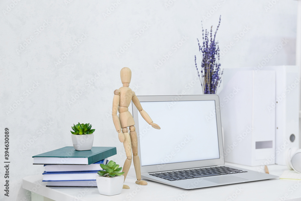 Modern workplace with laptop and wooden mannequin in office