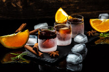 Frozen Herb Liqueur In Small Glass. Shot Glass Of Herb Liqueur With Cinnamon And Oranges On A Dark Background