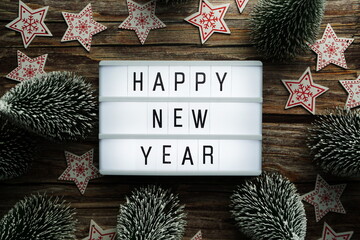 Wall Mural - Happy New Year word in light box with Christmas tree top view on wooden background