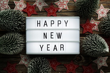 Wall Mural - Happy New Year word in light box with Christmas tree top view on wooden background