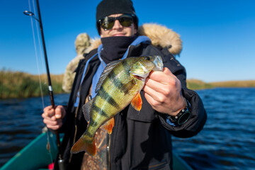 Wall Mural - Angler with fish. Amateur fisherman holds perch and stands with fishing rod in the boat on a river