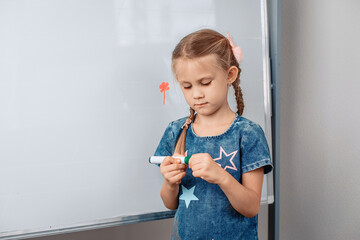 Portrait of a cute affectionate girl drawing a picture on a white board and opening a green marker to continue. Drawing concept.photo with noise