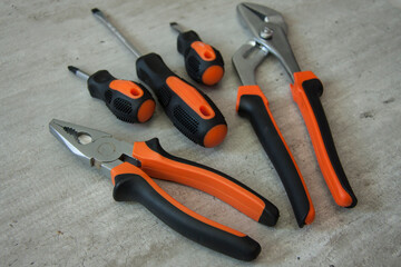 Construction and repair tools. Set on a wooden background. Metal screwdrivers and pliers with black and orange handles. Equipment for electrician, plumber and installer