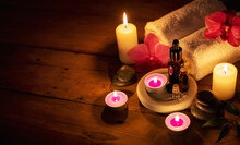 Romantic Spa - Essential Oils With Massage Stones And Flowers In Cadlelight On Wooden Background With Copy Space