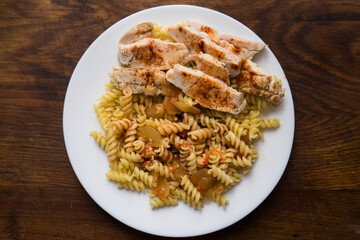 Fusilli with chicken. A plate with food on a wooden table. Fried chicken meat with spaghetti