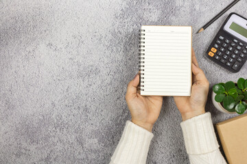 Wall Mural - A woman's hand holding a notebook with pencil and calculator on the desk.- Business concept.