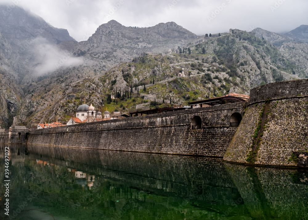 The well preserved city walls, which date back to the 17th and 17th centuries. The day is cloudy and there is fog. Kotor, Montenegro. - obrazy, fototapety, plakaty 