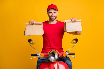 Photo of cheerful guy ride bike hold two paper packages wear red t-shirt headwear isolated yellow color background