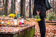 Mourning Woman Holding Flowers In Hands And Standing At Grave In Cemetery