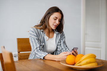 Pleased beautiful woman using cellphone while sitting at table