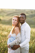 © Vadim Pastuh - Relaxed multiracial pregnant couple in the park outdoor. An african american husband hugs from the back his charming pregnant wife