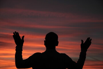 Wall Mural - praying to god with arms outstretched in the sky sunset stock photo