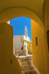 Wall Mural - A view through a covered alleyway towards a church tower in the village of Emporio, Santorini in summertime