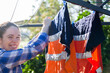 © Clare Seibel-Barnes/Austockphoto - Happy woman looking at camera and hanging reflective hi-vis work shirts to washing line