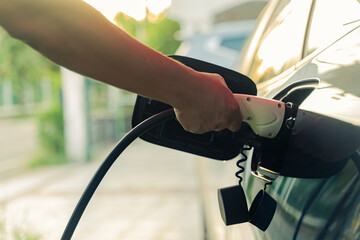 Man holding EV Car Plug-in hybrid car. Power supply connects to electric vehicle charge battery. Charging technology industry transport which is futuristic of the Automobile nature green energy