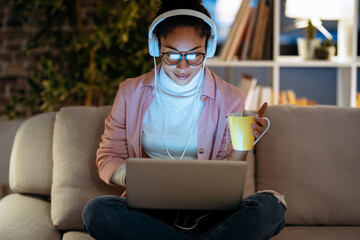 Beautiful young entrepreneur woman working with laptop while listening music with headphones sitting on couch in the office.