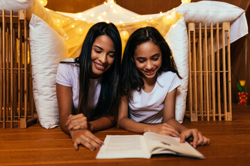 Wall Mural - Young latin mother and her daughter reading book at home