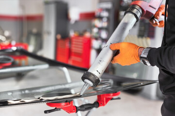 Glazier applying rubber sealing to windshield in garage, close up. High quality photo