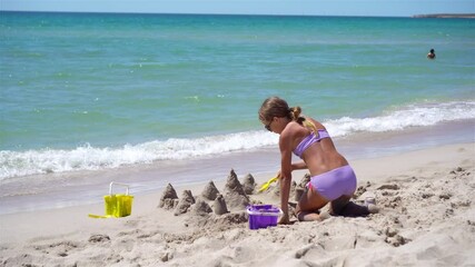 Wall Mural - Little girl at tropical white beach making sand castle