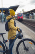 Vertical photo of a man in winter clothes, waiting with his bike, the train. In the background the train that is about to arrive.