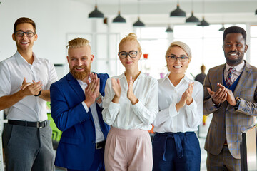 Wall Mural - portrait of positive interracial team looking at camera in the office, posing, young people have a good cooperation, stand clapping hands celebrating congratulating