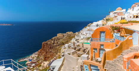 Wall Mural - The buildings of the village of Oia, Santorini tumble down the cliffside to the azure blue sea in the caldera in summertime
