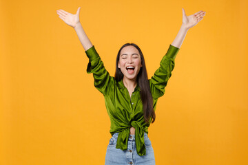 Wall Mural - Excited cheerful joyful happy young brunette asian woman 20s wearing basic green shirt standing rising spreading hands keeping eyes closed isolated on bright yellow colour background studio portrait.