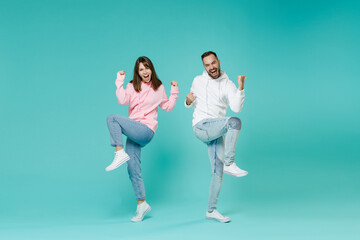 Wall Mural - Full length of overjoyed screaming young couple two friends man woman 20s in white pink casual hoodie doing winner gesture clenching fists isolated on blue turquoise wall background studio portrait.