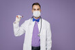 © ViDi Studio - Young doctor man in white medical gown face mask safe from coronavirus virus covid-19 hold blood test result sample tube isolated on violet background. Healthcare personnel health medicine concept.