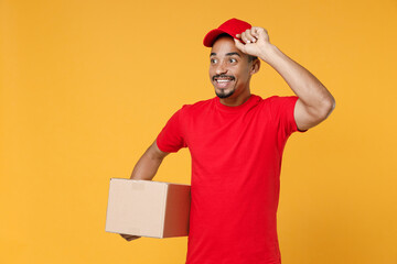 Wall Mural - Delivery employee african man 20s in red cap blank print t-shirt uniform work courier service on quarantine coronavirus covid-19 virus concept hold cardboard box isolated on yellow background studio.