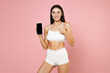 © ViDi Studio - Smiling attractive sexy young brunette woman 20s in white underwear posing hold mobile cell phone with blank empty screen showing thumb up isolated on pastel pink colour background studio portrait.