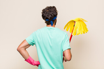 Wall Mural - young man feeling confused or full or doubts and questions, wondering, with hands on hips, rear view