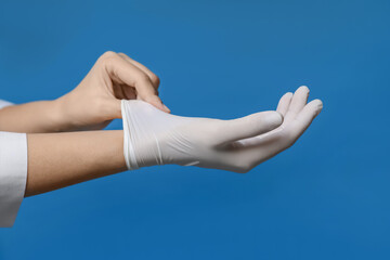 Wall Mural - Doctor putting on medical gloves against blue background, closeup