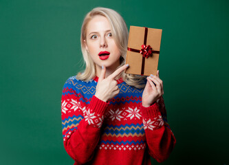 Wall Mural - Beautiful woman in Christmas sweater with gift box on green background